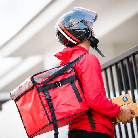 Kurier in roter Uniform Zusteller steht mit Paketen in den Händen im Freien warten Hausbesitzer offene Tür