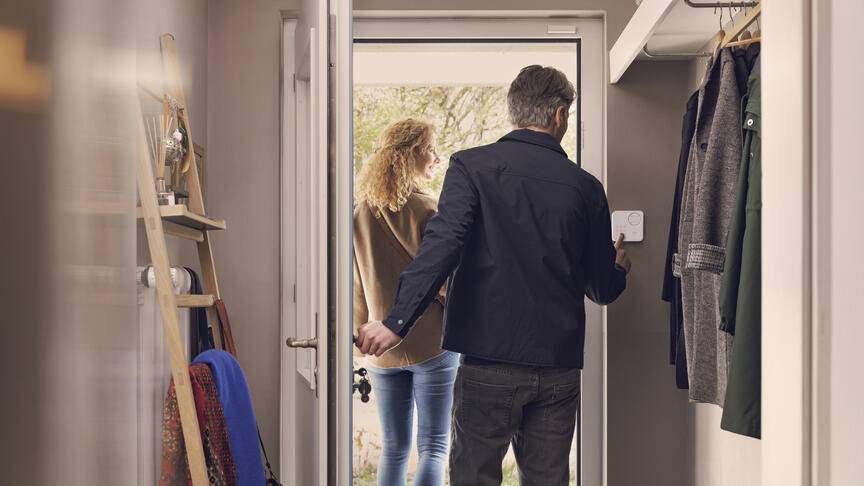 Paar verlässt Zuhause. Mann schaltet Alarmanlage an.